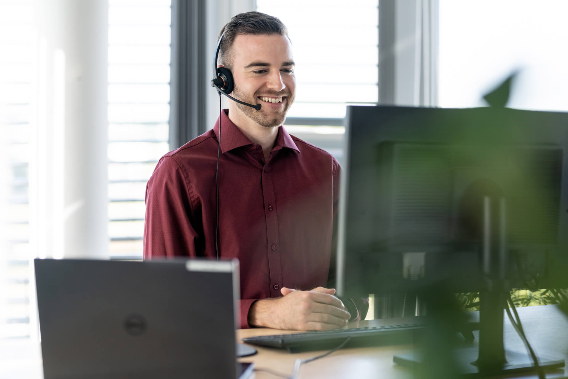 Translator sitting in front of a PC and keyboard with headset, smiling.