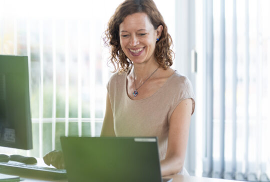 Native speaker expert translating, smiling, in the office with a laptop.